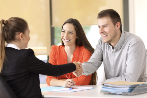 A young couple shaking hands with a woman in professional dress