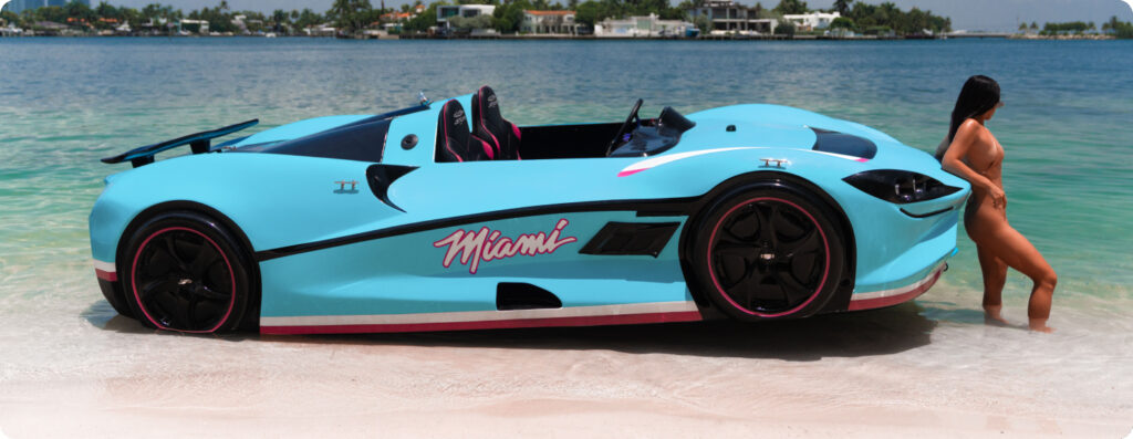 Light Blue luxury watersports car, two seats, speed boat, sitting on the shore. Series X with a lady standing in front of the boat. Available at Pier One Yacht Sales